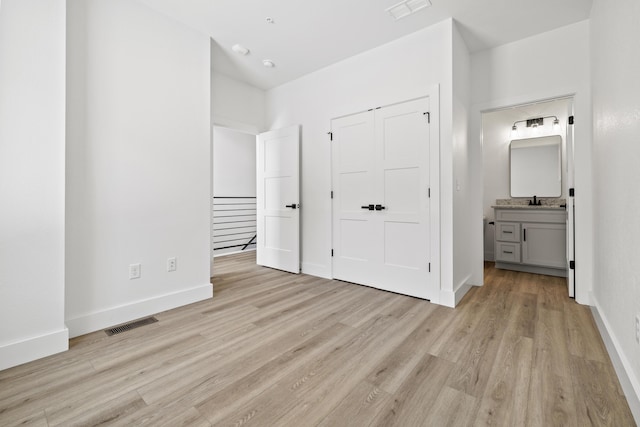 unfurnished bedroom featuring light wood-type flooring, visible vents, connected bathroom, and baseboards