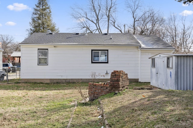 rear view of property featuring a shingled roof, a lawn, fence, an outdoor structure, and a shed