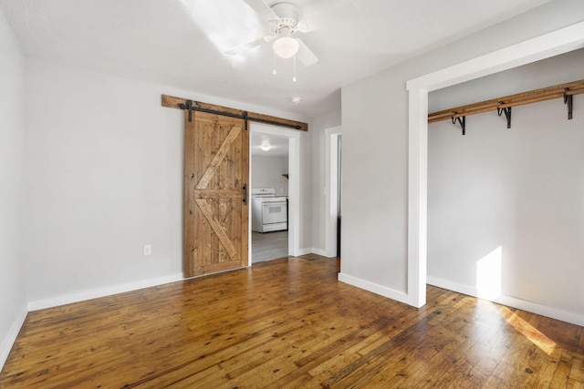 unfurnished bedroom with a barn door, hardwood / wood-style flooring, a ceiling fan, baseboards, and a closet