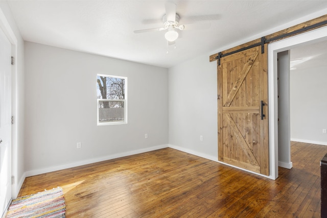 unfurnished bedroom with baseboards, ceiling fan, hardwood / wood-style floors, and a barn door