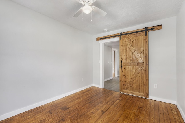 spare room with wood-type flooring, ceiling fan, baseboards, and a barn door