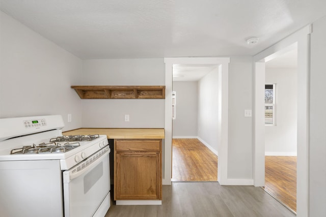 kitchen with baseboards, white range with gas cooktop, open shelves, light wood finished floors, and brown cabinetry