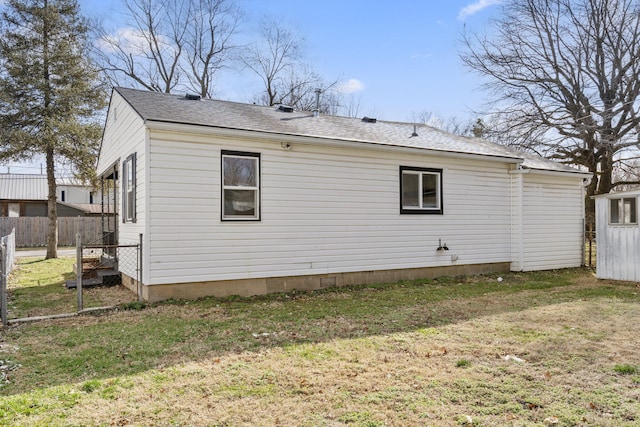 rear view of property with a shingled roof, fence, and a yard