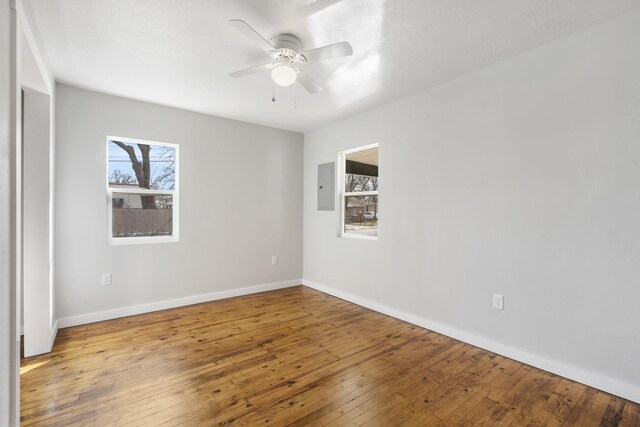 empty room featuring ceiling fan, hardwood / wood-style flooring, electric panel, and baseboards