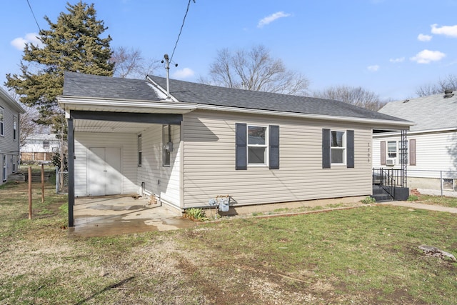 rear view of house featuring a shingled roof, a lawn, and fence