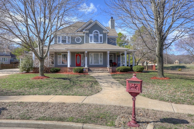 view of front facade with covered porch, a chimney, a front lawn, and roof with shingles