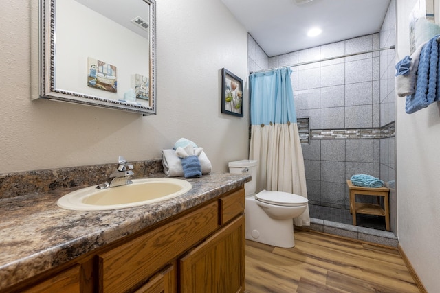 full bathroom with visible vents, toilet, wood finished floors, a tile shower, and vanity