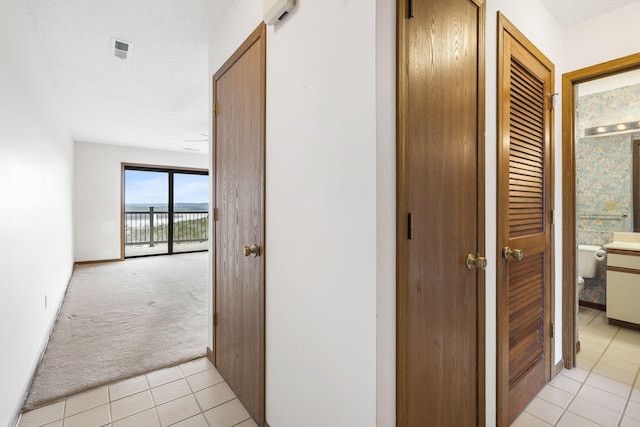 corridor with light carpet, light tile patterned floors, baseboards, and visible vents