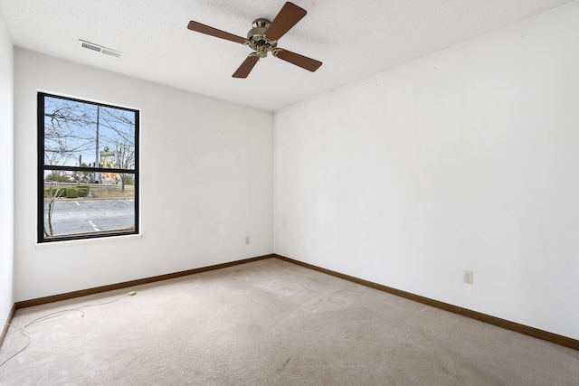 carpeted empty room featuring a textured ceiling, ceiling fan, visible vents, and baseboards