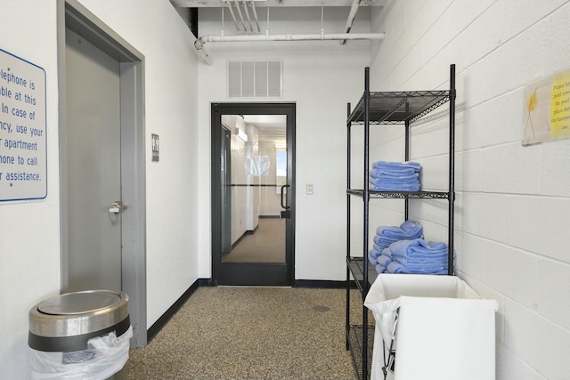 hall featuring concrete block wall, visible vents, and baseboards