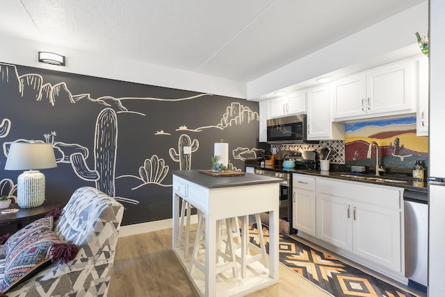 kitchen with dark countertops, white cabinetry, stainless steel appliances, and a sink