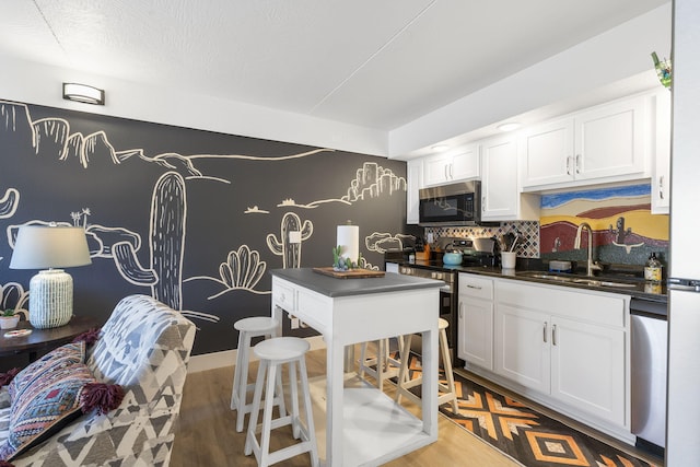 kitchen with white cabinets, dark countertops, stainless steel appliances, light wood-style floors, and a sink