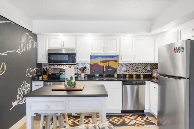 kitchen featuring appliances with stainless steel finishes, dark countertops, a sink, and white cabinets