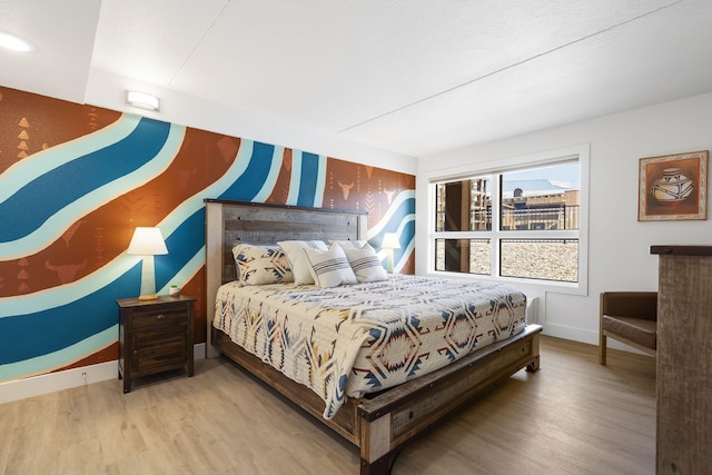 bedroom with an accent wall, wood finished floors, wallpapered walls, and baseboards