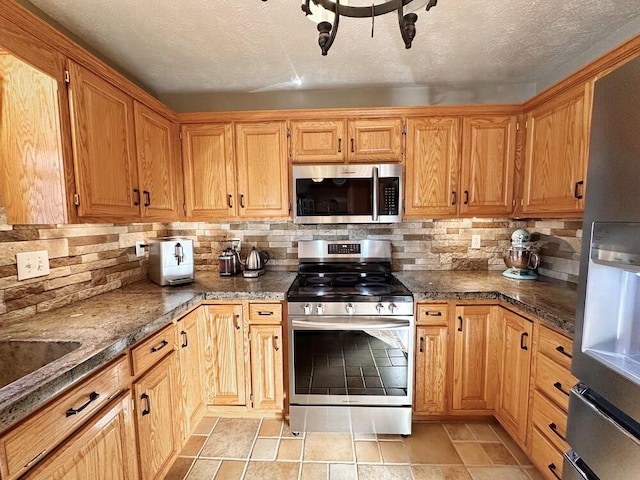 kitchen featuring appliances with stainless steel finishes, dark stone countertops, a textured ceiling, and decorative backsplash