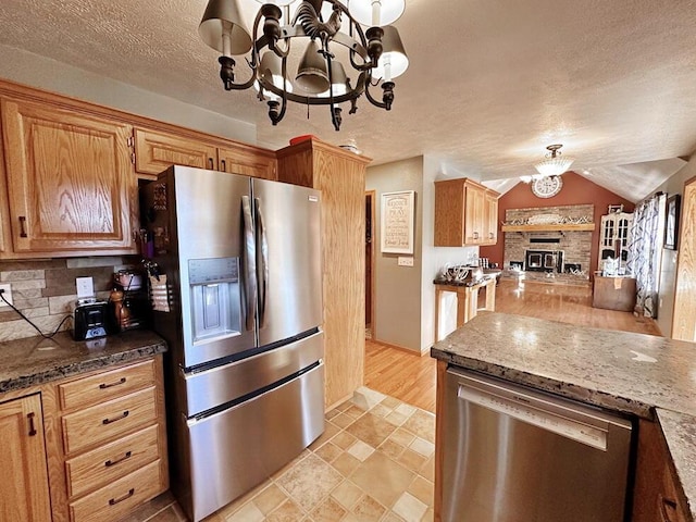 kitchen with decorative backsplash, appliances with stainless steel finishes, dark stone countertops, a textured ceiling, and a notable chandelier