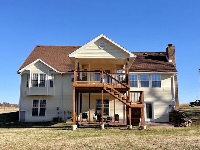 back of house with a chimney, central air condition unit, a shingled roof, a lawn, and stairway