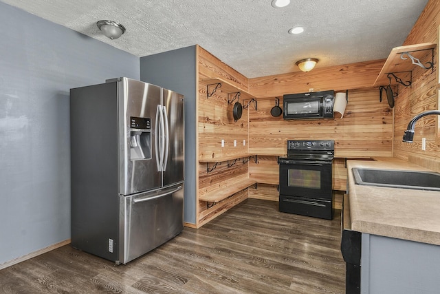 kitchen featuring dark wood-style flooring, a sink, wooden walls, and black appliances