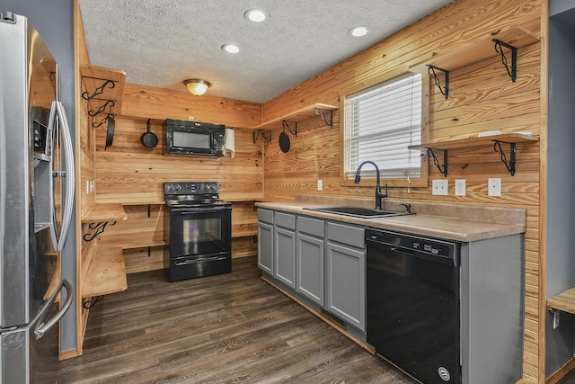 kitchen with gray cabinets, a sink, wooden walls, and black appliances