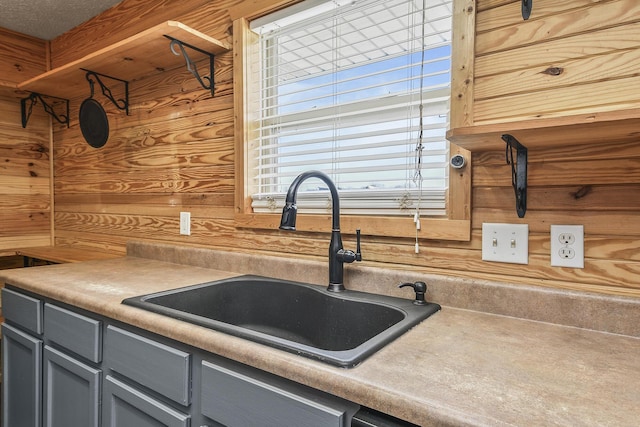 kitchen featuring light countertops, a sink, wooden walls, and gray cabinetry