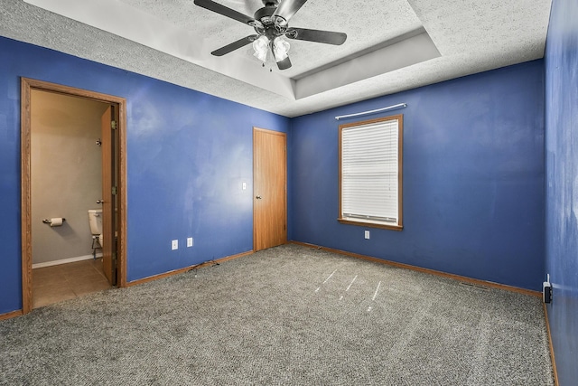 unfurnished bedroom featuring baseboards, a textured ceiling, a tray ceiling, and carpet flooring