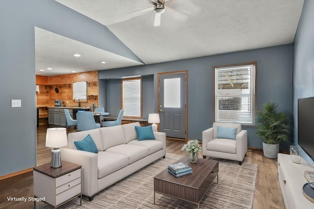 living area with lofted ceiling, a textured ceiling, wood finished floors, a ceiling fan, and baseboards