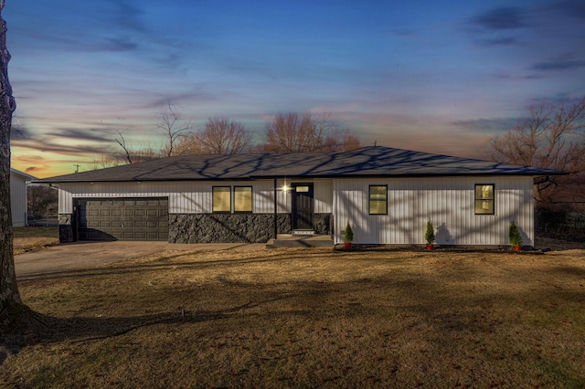 back of property with driveway, an attached garage, and a lawn