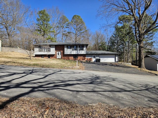 split foyer home featuring aphalt driveway, brick siding, and fence