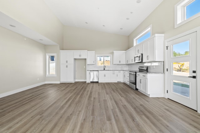 kitchen with stainless steel appliances, white cabinets, decorative backsplash, and a high ceiling