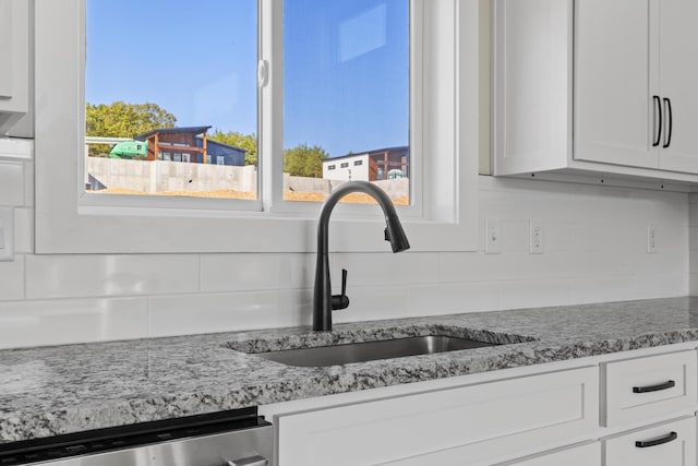 interior details with tasteful backsplash, white cabinets, a sink, light stone countertops, and dishwasher