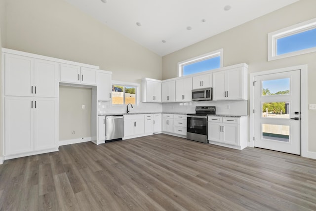 kitchen featuring white cabinets, appliances with stainless steel finishes, wood finished floors, high vaulted ceiling, and a sink