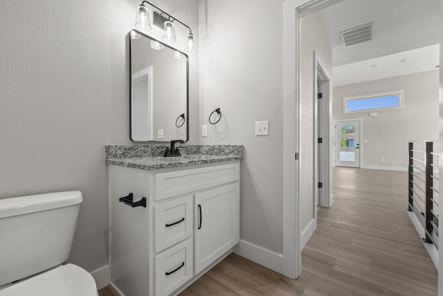 half bath with baseboards, visible vents, toilet, and wood finished floors