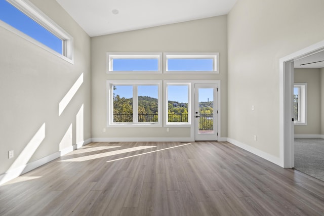 unfurnished living room featuring high vaulted ceiling, wood finished floors, and baseboards