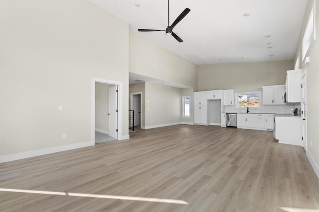 unfurnished living room with high vaulted ceiling, light wood finished floors, a sink, and a ceiling fan