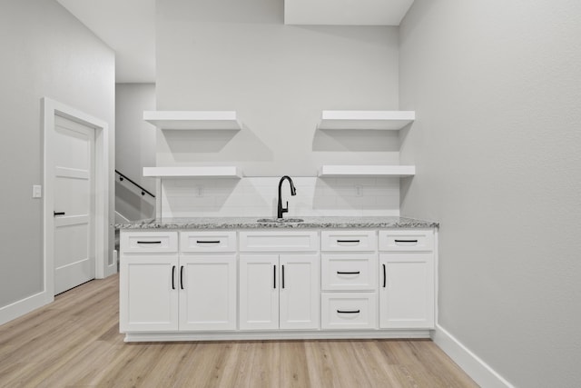 kitchen with light wood-type flooring, light stone countertops, a sink, and open shelves