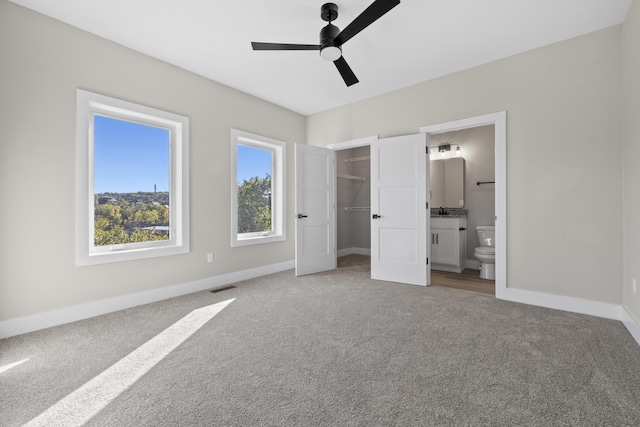 unfurnished bedroom with a walk in closet, visible vents, ensuite bathroom, light carpet, and baseboards