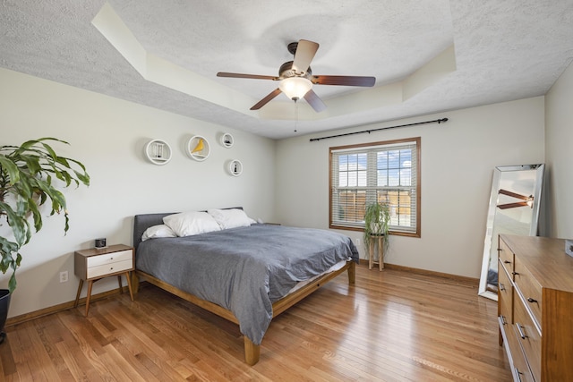 bedroom featuring baseboards, a ceiling fan, a tray ceiling, a textured ceiling, and light wood-style floors