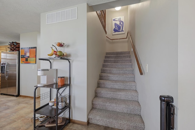 stairs with baseboards, visible vents, and a textured ceiling