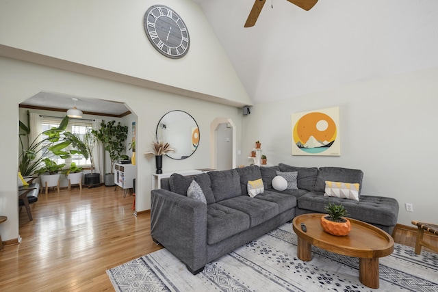 living room with light wood-type flooring, arched walkways, high vaulted ceiling, and a ceiling fan