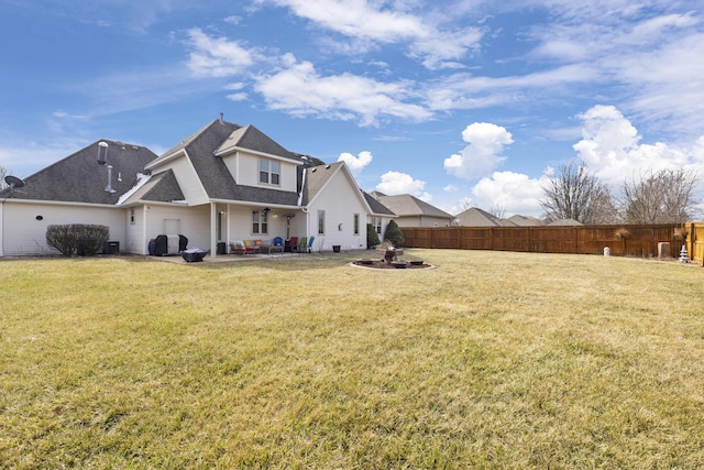 rear view of property featuring a shingled roof, a patio area, fence, and a lawn