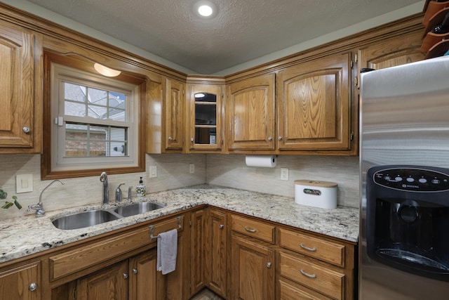 kitchen featuring brown cabinets, decorative backsplash, stainless steel refrigerator with ice dispenser, and a sink