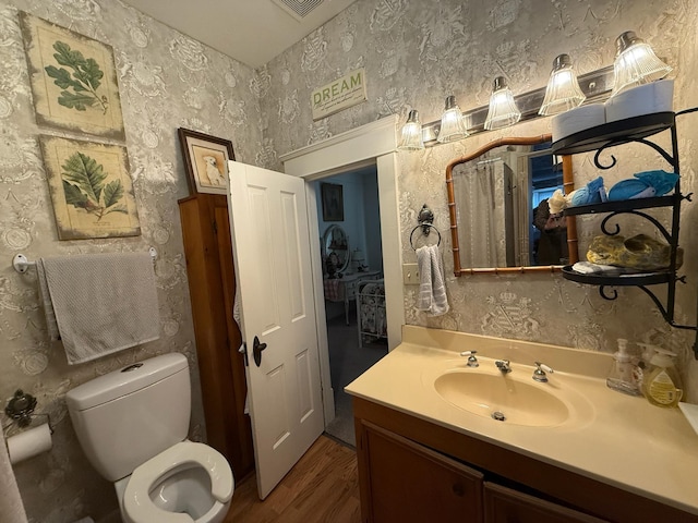 half bath featuring vanity, toilet, and wallpapered walls