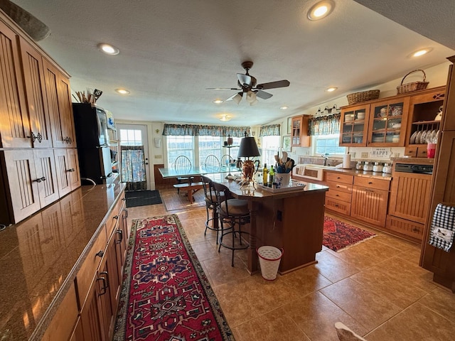 kitchen featuring glass insert cabinets, a breakfast bar area, brown cabinets, light tile patterned flooring, and recessed lighting