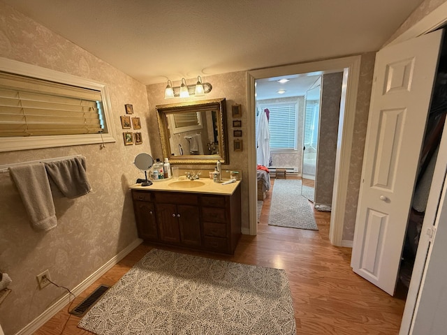 bathroom featuring vanity, wood finished floors, visible vents, and wallpapered walls