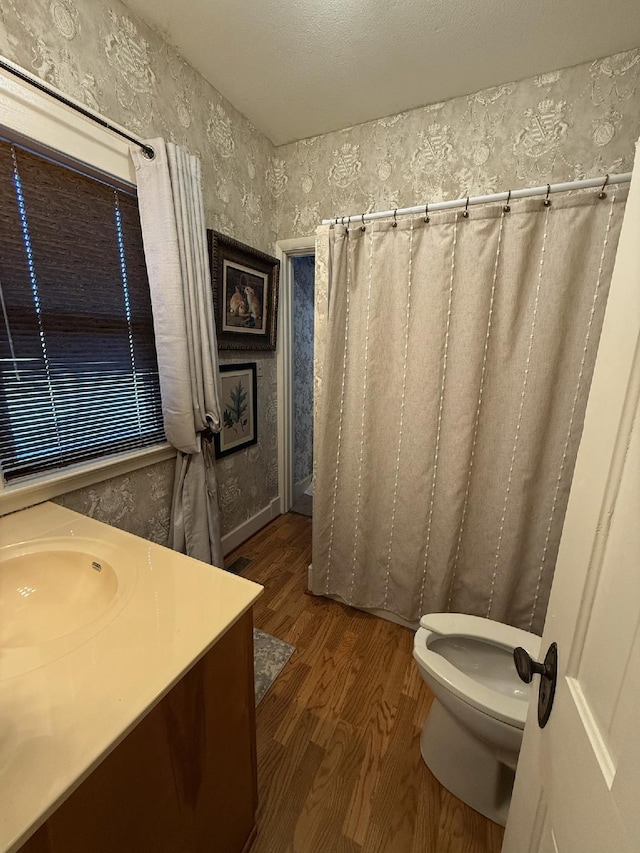 bathroom featuring toilet, a shower with shower curtain, wood finished floors, vanity, and wallpapered walls