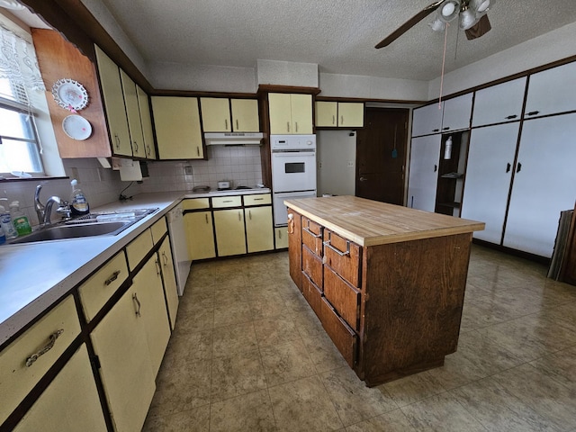 kitchen featuring under cabinet range hood, white appliances, a kitchen island, a sink, and decorative backsplash