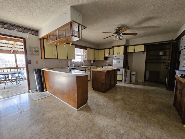 kitchen with double oven, a ceiling fan, a kitchen island, a peninsula, and under cabinet range hood