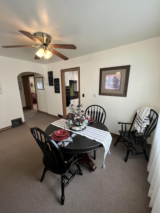 carpeted dining area featuring arched walkways, a ceiling fan, and baseboards