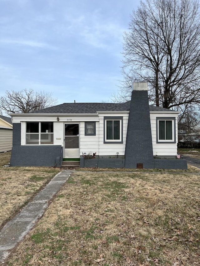 view of front facade featuring a shingled roof, a chimney, and a front yard