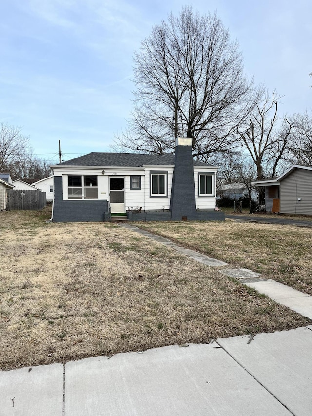 view of front facade with entry steps, a shingled roof, a chimney, fence, and a front yard